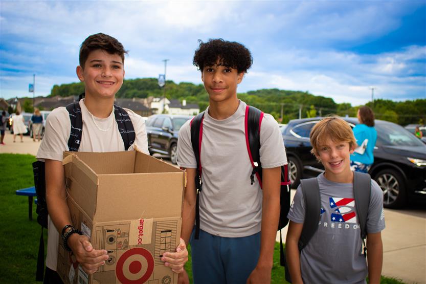 Students smile while holding a box of school supplies